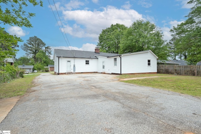 view of front facade with fence, driveway, a chimney, and a front lawn