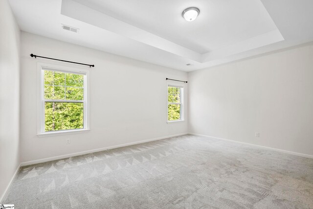 carpeted spare room with baseboards, a raised ceiling, and visible vents