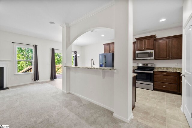 kitchen with dark brown cabinetry, appliances with stainless steel finishes, arched walkways, baseboards, and light stone counters