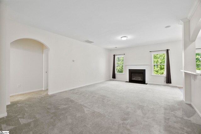 unfurnished living room with light colored carpet, a fireplace with flush hearth, baseboards, and visible vents