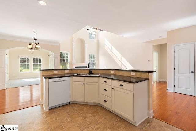 kitchen featuring white dishwasher, arched walkways, dark countertops, a sink, and open floor plan