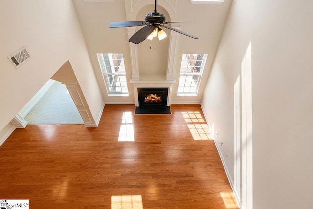 unfurnished living room featuring visible vents, light wood-style floors, baseboards, a high ceiling, and a ceiling fan