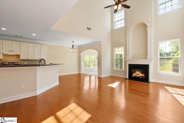 unfurnished living room with visible vents, a fireplace with flush hearth, ceiling fan with notable chandelier, light wood finished floors, and a high ceiling
