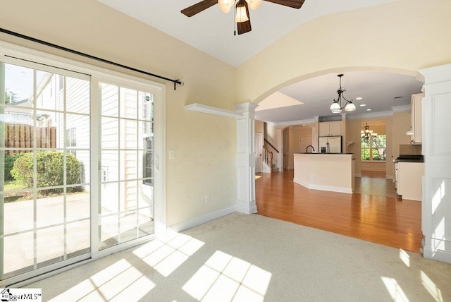 interior space with baseboards, light colored carpet, ornate columns, arched walkways, and ceiling fan with notable chandelier