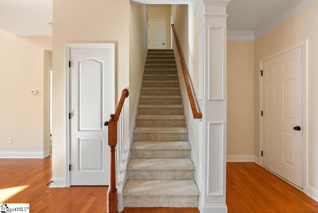 stairs with crown molding, ornate columns, baseboards, and wood finished floors