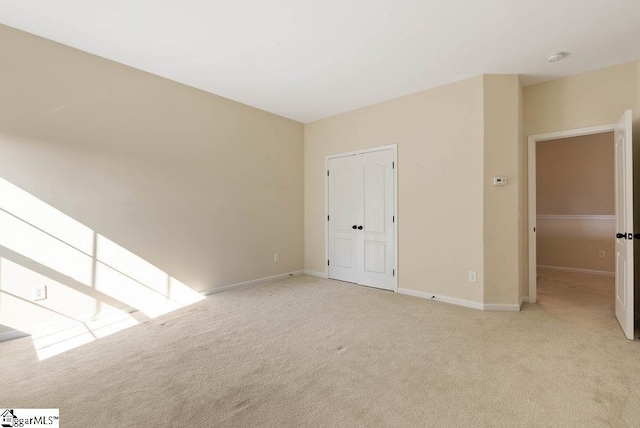 empty room featuring baseboards and light carpet
