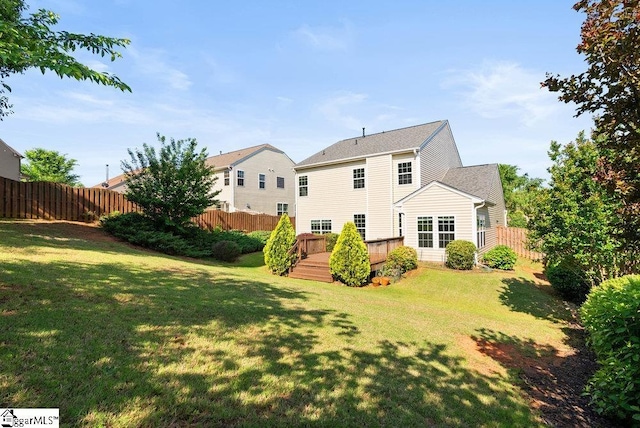 rear view of property featuring fence, a wooden deck, and a lawn