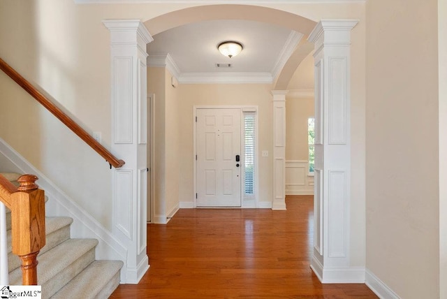 entrance foyer featuring arched walkways, wood finished floors, stairway, ornamental molding, and ornate columns