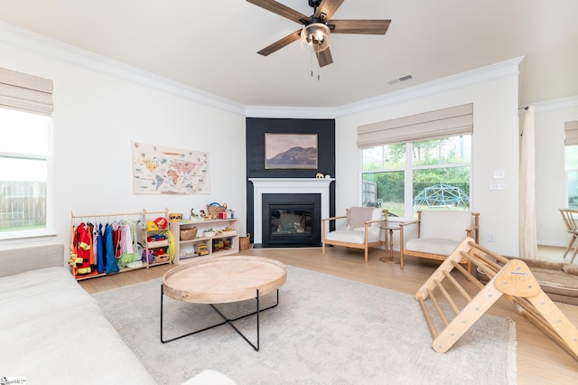 living room with visible vents, ornamental molding, a glass covered fireplace, wood finished floors, and ceiling fan