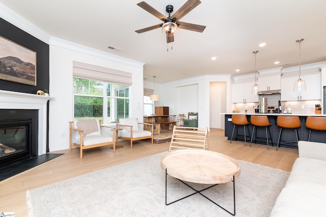 living room with a ceiling fan, visible vents, ornamental molding, and light wood-style flooring