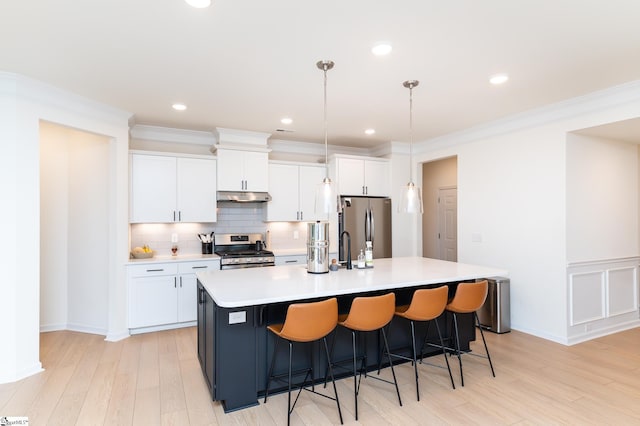 kitchen with a center island with sink, light countertops, under cabinet range hood, white cabinets, and stainless steel appliances