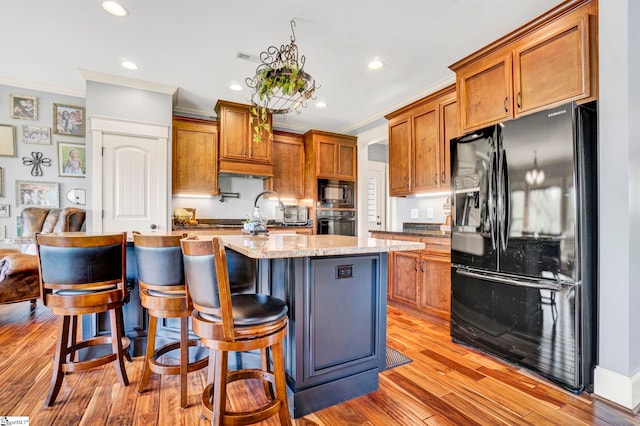 kitchen with crown molding, light wood-style floors, brown cabinetry, and black appliances