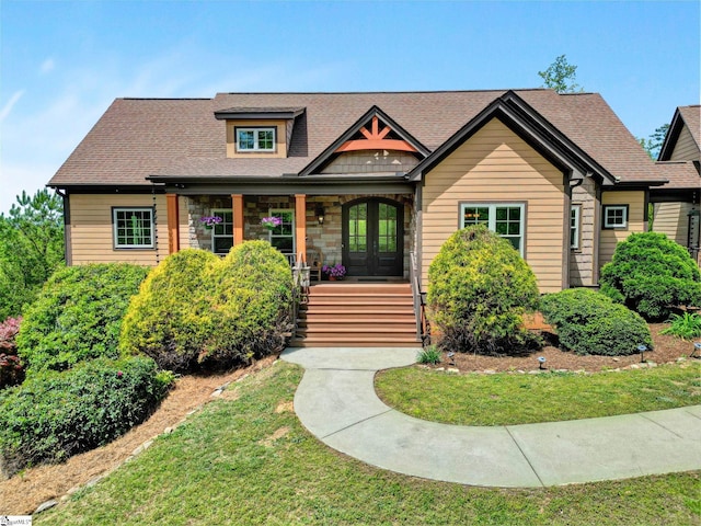 view of front of home featuring roof with shingles, stone siding, a porch, a front yard, and french doors