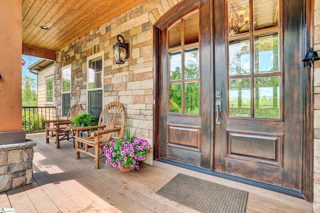 doorway to property with french doors, a porch, and stone siding