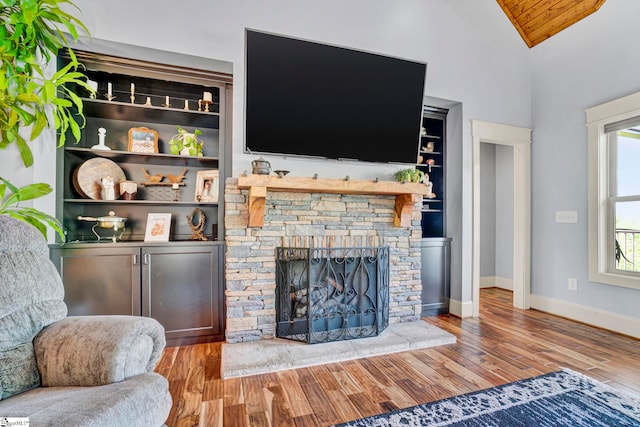 living room with a stone fireplace, wood finished floors, wooden ceiling, baseboards, and lofted ceiling