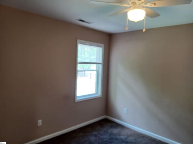 spare room featuring ceiling fan, dark carpet, and baseboards