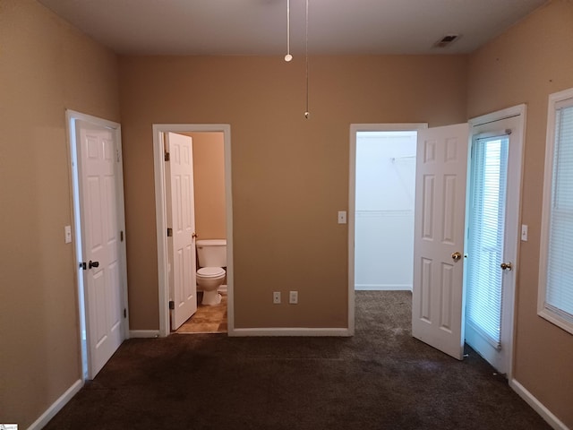 unfurnished bedroom featuring a walk in closet, dark colored carpet, connected bathroom, and baseboards