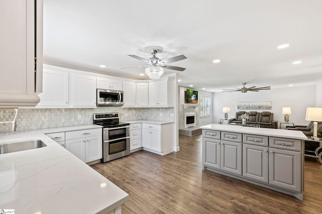 kitchen with a large fireplace, stainless steel appliances, open floor plan, a ceiling fan, and decorative backsplash