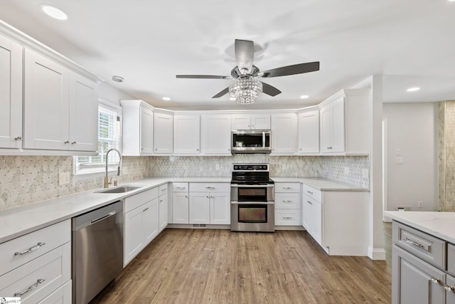 kitchen featuring a ceiling fan, appliances with stainless steel finishes, white cabinetry, a sink, and light wood-style flooring