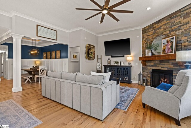 living room featuring ceiling fan, a fireplace, decorative columns, wood finished floors, and ornamental molding