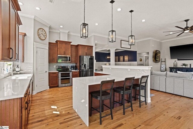 kitchen with ornate columns, open floor plan, appliances with stainless steel finishes, and ornamental molding