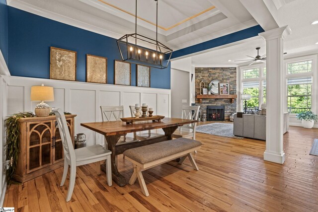 dining room featuring decorative columns, a ceiling fan, a stone fireplace, light wood finished floors, and a decorative wall