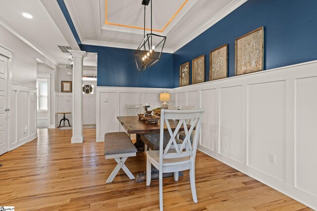 dining space with ornate columns, ornamental molding, a raised ceiling, and a decorative wall