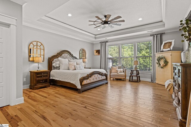 bedroom with recessed lighting, a tray ceiling, and light wood-style flooring