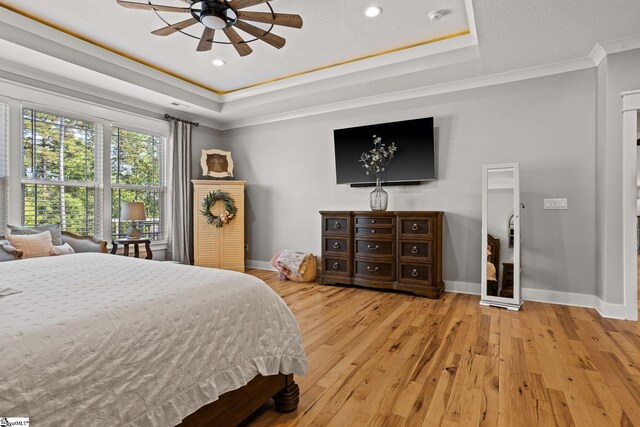 bedroom featuring crown molding, a tray ceiling, baseboards, and wood finished floors
