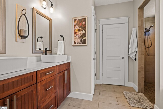 full bath with tile patterned flooring, double vanity, baseboards, walk in shower, and a sink