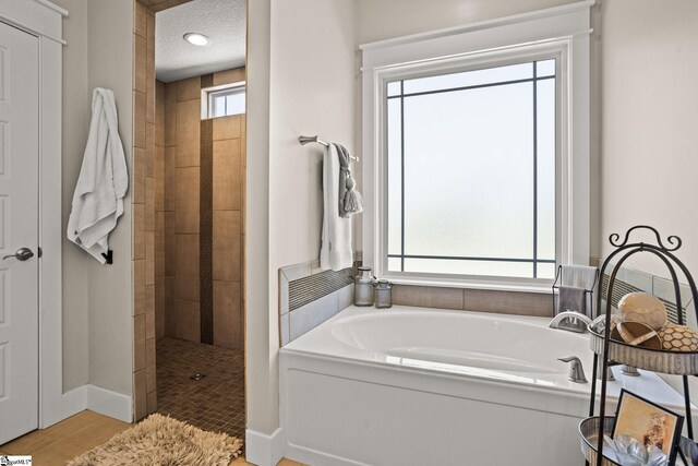 bathroom with a textured ceiling, a tile shower, baseboards, and a garden tub