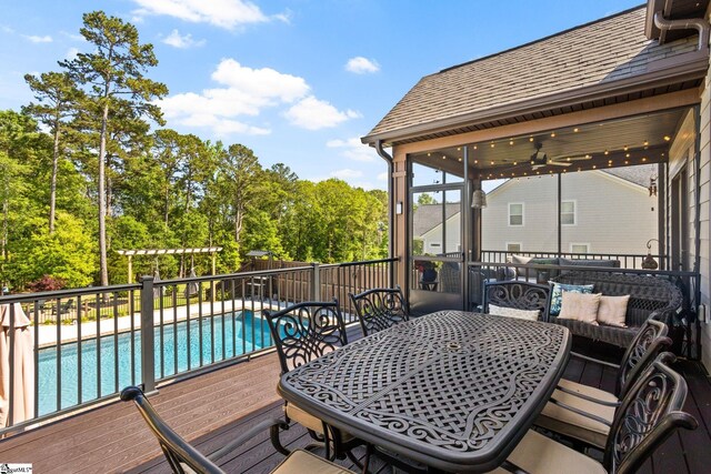 wooden deck with outdoor dining area, ceiling fan, and a fenced in pool