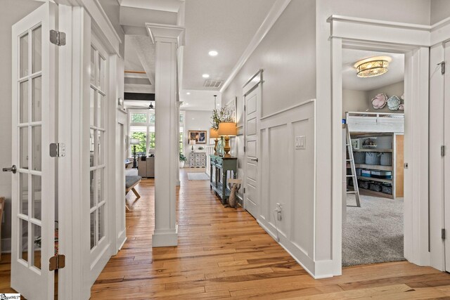 hall with ornate columns, ornamental molding, french doors, and light wood-type flooring