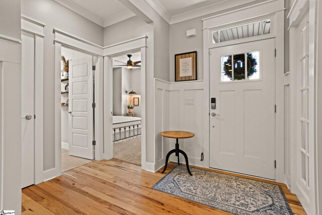 foyer with light wood-style floors, ornamental molding, wainscoting, and a ceiling fan