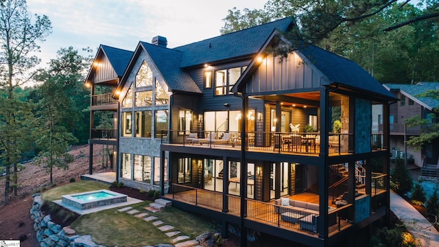 rear view of house featuring a shingled roof, stone siding, board and batten siding, a deck, and a balcony