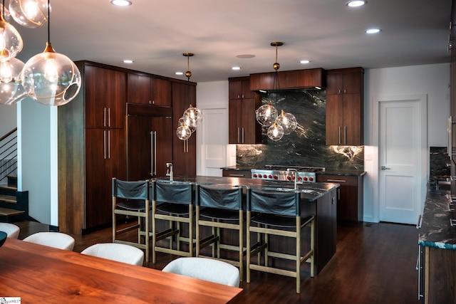 kitchen with hanging light fixtures, an island with sink, recessed lighting, tasteful backsplash, and dark wood-style floors