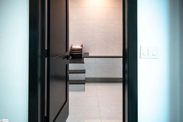 hall with light tile patterned flooring and tile walls
