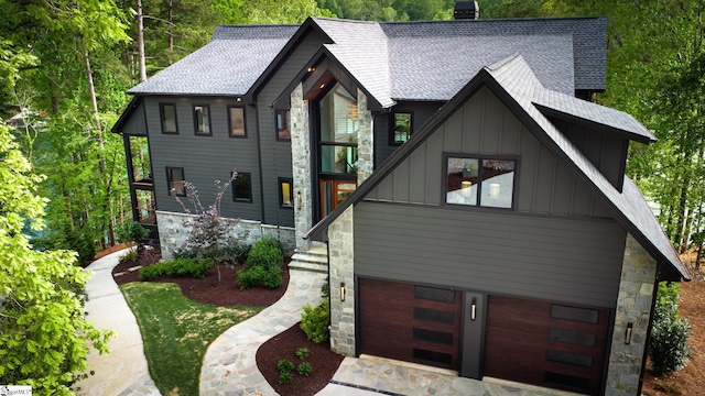 view of front facade featuring board and batten siding, an attached garage, a shingled roof, and stone siding