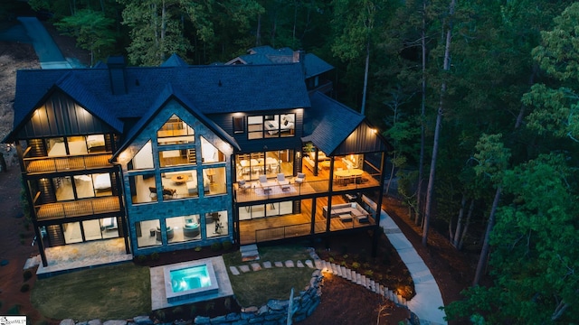 rear view of property with roof with shingles, a forest view, a patio area, and a balcony