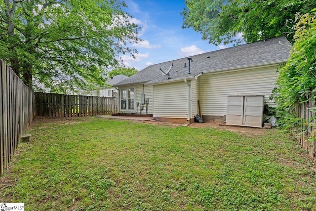 back of house featuring a lawn, a fenced backyard, and roof with shingles