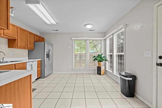 kitchen with brown cabinets, a sink, dishwasher, light countertops, and a textured ceiling