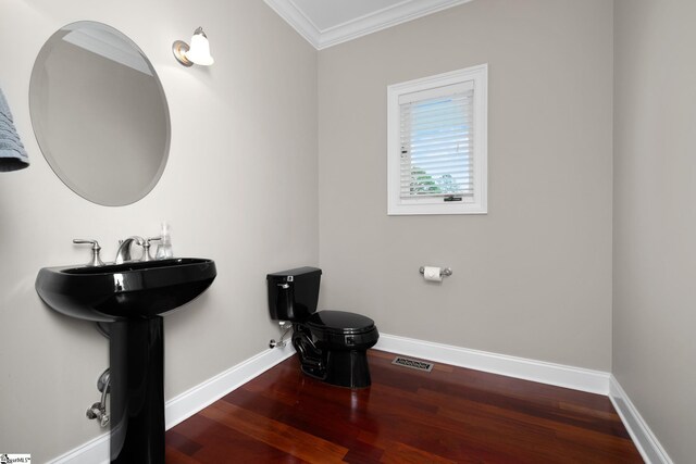 half bath with visible vents, crown molding, wood finished floors, baseboards, and toilet