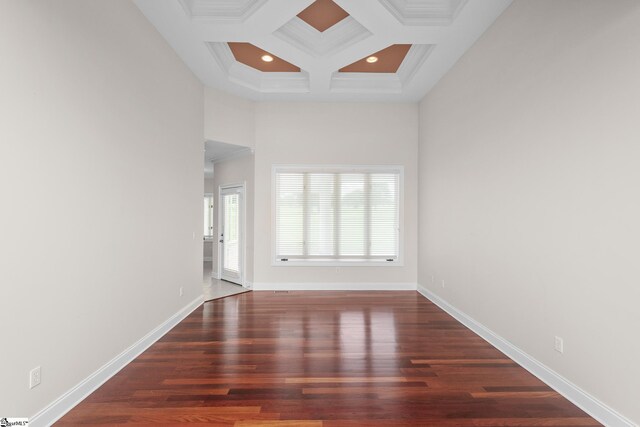 empty room featuring wood finished floors, baseboards, beamed ceiling, ornamental molding, and coffered ceiling