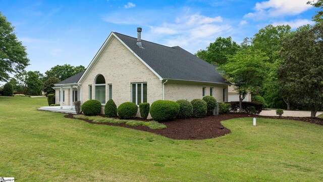 view of side of property with brick siding, a shingled roof, a garage, and a yard