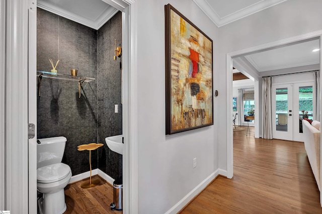 half bath with baseboards, ornamental molding, wood finished floors, and toilet