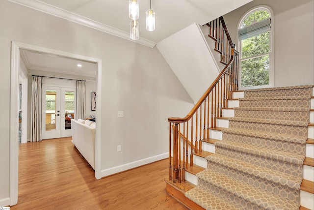 staircase with crown molding, wood finished floors, a wealth of natural light, and french doors