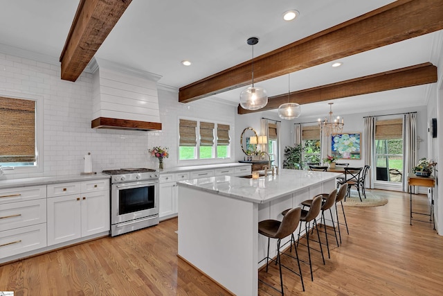 kitchen with stainless steel range with gas stovetop, light wood-style floors, white cabinets, and beamed ceiling