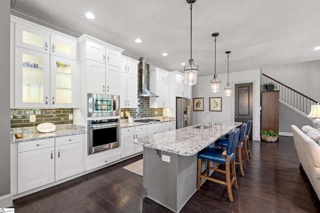 kitchen featuring a breakfast bar area, wall chimney range hood, a sink, backsplash, and stainless steel appliances