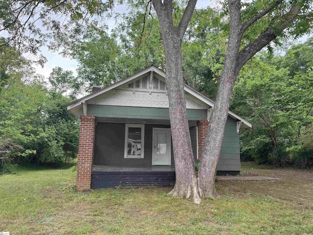 exterior space with covered porch, a chimney, and a front lawn