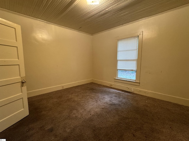 empty room with baseboards, wood ceiling, and dark colored carpet